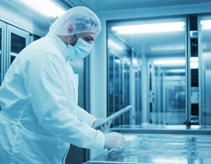 Technician in cleanroom suit examining semiconductor wafers in advanced manufacturing facility