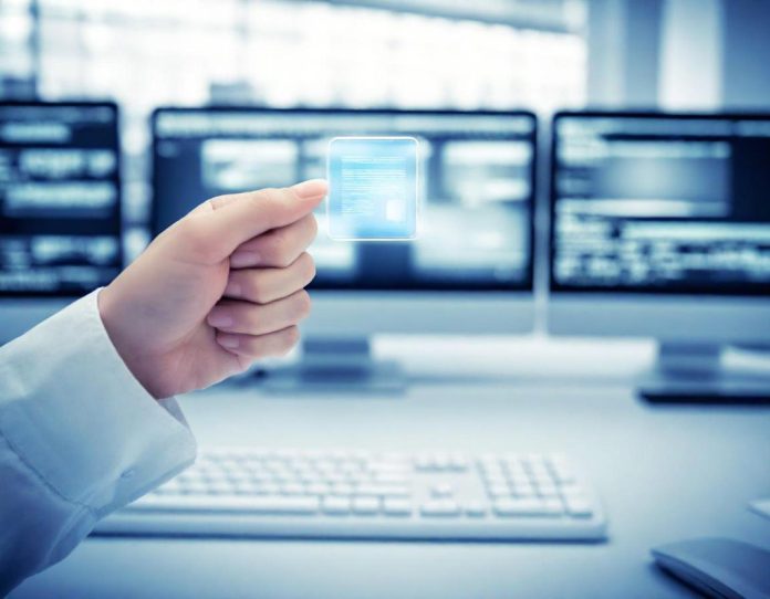 Close-up of a hand pressing delete key on keyboard with blurred computer screens in background